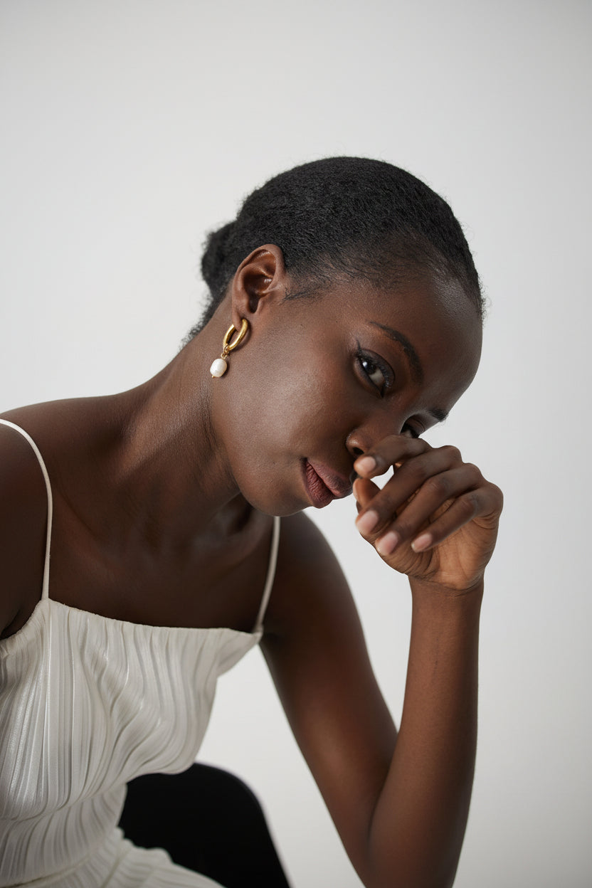 Woman wearing gold and pearl earrings with a neutral background
